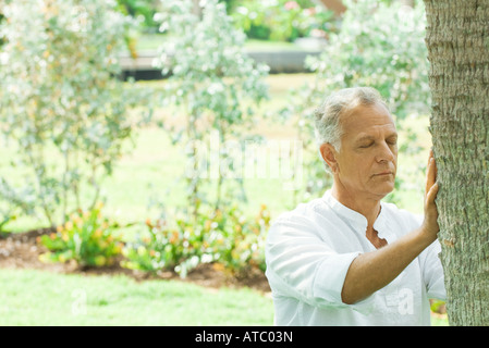Mature man touching tree trunk, eyes closed Stock Photo