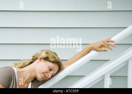 Woman leaning against railing, head resting on arm, smiling, side view Stock Photo
