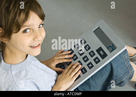 Little boy sitting on the ground, playing with large calculator, smiling at camera Stock Photo