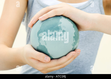 Woman holding globe in cupped hands, close-up, cropped view Stock Photo