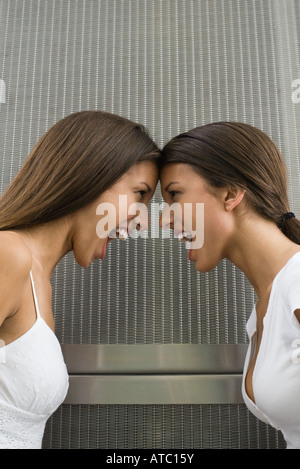 Twin sisters face to face, touching foreheads, mouths open, side view Stock Photo