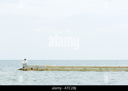 Man sitting at the end of pier, reading book, in the distance Stock Photo