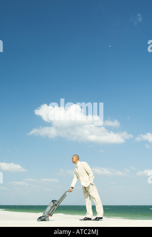 Man in suit using vacuum cleaner on beach, full length Stock Photo