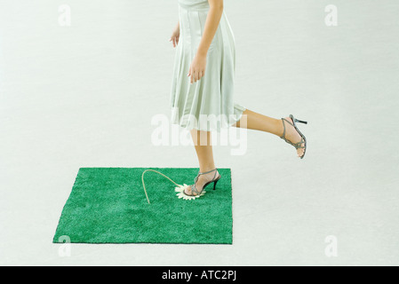 Woman stepping on flower in square of artificial turf, waist down Stock Photo