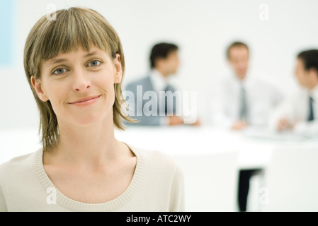 Businesswoman smiling at camera, portrait, businessmen in background Stock Photo