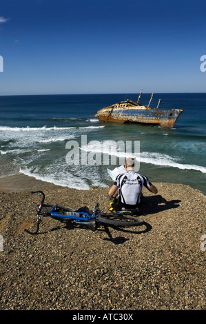 bicyclist sitting by the boat wreck of the American star in Fuerteventura Spain reading a map by the sea. Stock Photo