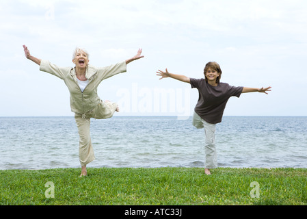 Grandmother and grandson standing on one leg, arms outstretched, both smiling at camera Stock Photo