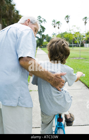 Grandfather teaching grandson to ride bicycle, rear view Stock Photo