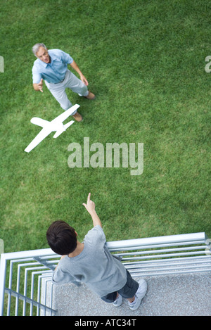 Boy standing on balcony, throwing toy airplane to grandfather standing below, high angle view Stock Photo