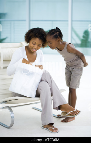 Woman sitting in chair, holding gift bag, daughter standing beside her, both looking down Stock Photo