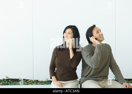 Couple sitting side by side, both using cell phones Stock Photo