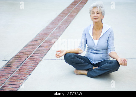 Senior woman sitting in lotus position, eyes closed Stock Photo