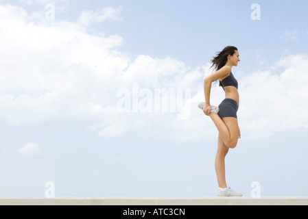 Young woman in sports clothing standing, holding one foot in hand, side view Stock Photo