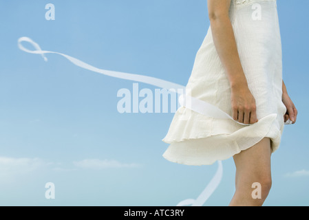 Woman in dress holding ribbon, tousled by wind, cropped view Stock Photo