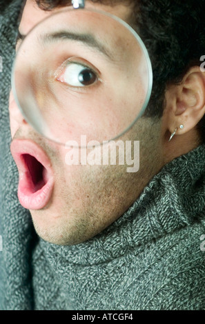 Portrait of Latino man peering through magnifying glass Stock Photo