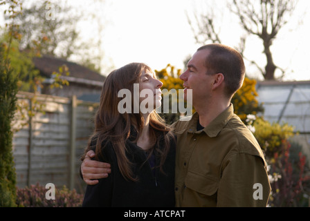 Loving couple looking each other in the eye in their back garden, wife wearing a wig due to chemotherapy. Stock Photo