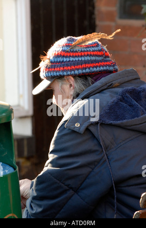 a homeless person man wearing a tea cosy bobble hat made of wool woolen with a pheasant feather in his cap Stock Photo