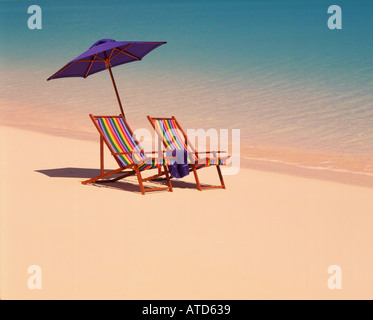 Tropical scene of two colorful beach chairs and an umbrella sitting at waters edge in the Bahamas Stock Photo