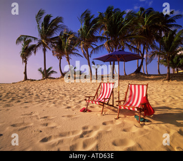 Two colorful beach chairs and an umbrella sit in the pristine white sand of a beach in the Bahamas Stock Photo
