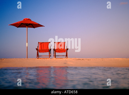Red beach chairs and umbrella sit on a beach in the Bahamas facing the Caribbean sea Stock Photo