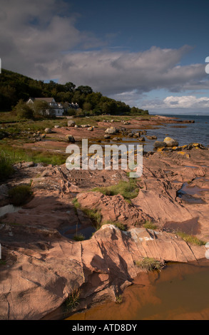 vertical landscape photo of patterns in sandstone rock at Pirates Cove with the village of Corrie behind on the Isle of Arran Stock Photo