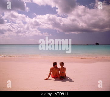 A couple sitting side by side in the pristine pink sand of Horseshoe Bay beach in Bermuda Stock Photo