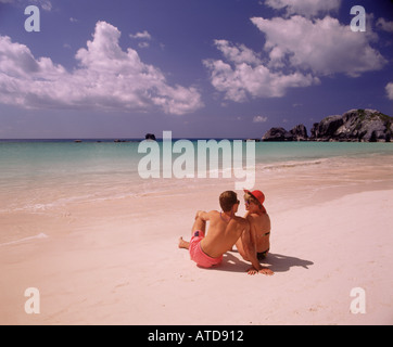 A couple sitting side by side in the pristine pink sand of Horseshoe Bay beach in Bermuda Stock Photo