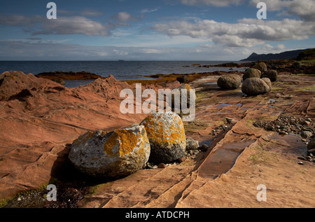 granite boulders on sandstone bedrock on the shore at Corrie on the Isle of Arran in scotland with Holy Island in the distance Stock Photo