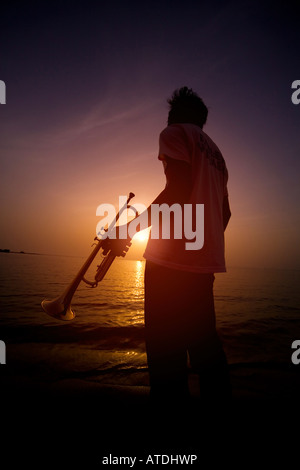 Silhouette of young man holding trumpet by lake Stock Photo