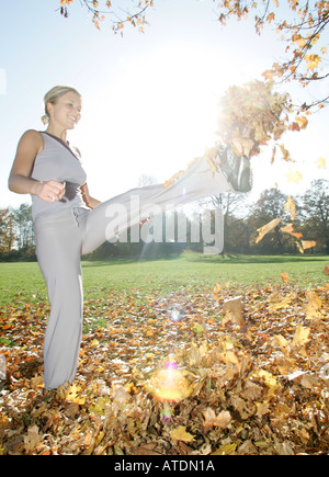 young woman kicking into a pile of leaves in the park Stock Photo