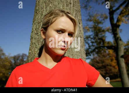 Portrait of a young blonde woman leaning against tree trunk taking a rest after exercising Stock Photo
