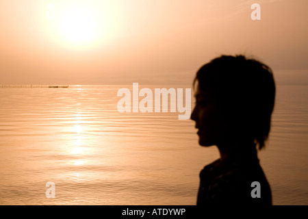 Silhouette of young woman looking at lake Stock Photo