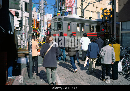 Locals wait at an automatic level crossing in Tokyo's Jiyugaoka for a commuter rapid express train to pass. Stock Photo