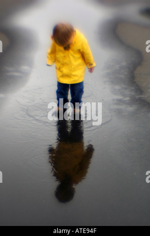 Small boy playing in puddle of water rain slicker Stock Photo