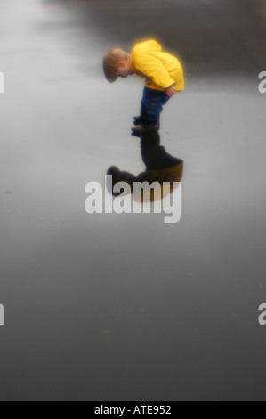 Small boy playing in puddle of water rain slicker and reflection Stock Photo