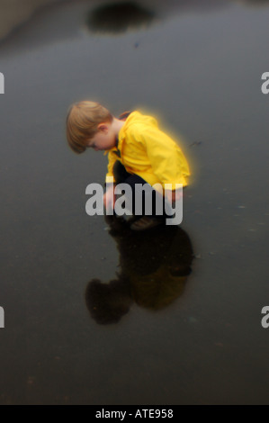 Small boy playing in puddle of water wearing yellow rain jacket Stock Photo