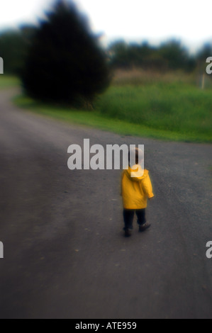 future concept Small boy walking down long roadway wearing yellow coat Stock Photo