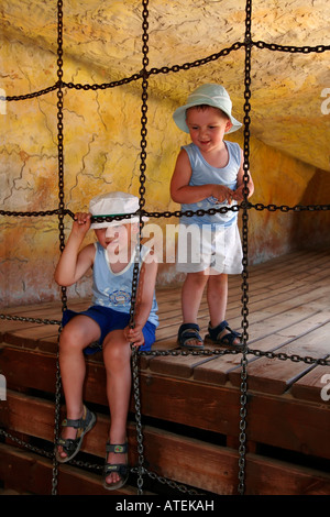 Young boys sitting on ledge near chain links, kids play in cave on playground Stock Photo