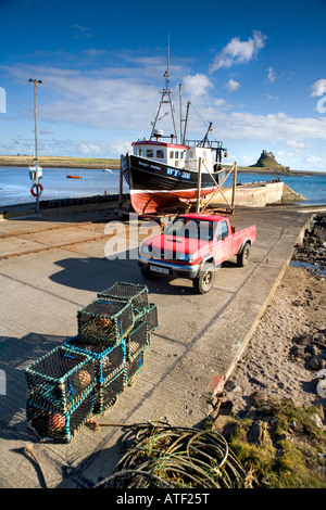 A fishing boat and crab pots on the jetty with Lindisfarne Castle on Holy Island, Northumberland, England, UK Stock Photo