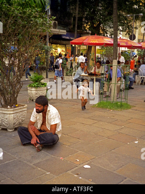 Beggar man sit on floor in busy posh boulevard as people go pass by have coffee Rio de Janeiro Brazil Brasil South Latin America Stock Photo