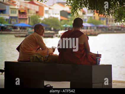 Pair of novices in colourful traditional robe sitting public bench by river creek drinking pepsi Singapore Southeast Asia Stock Photo