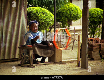 Senile indigenous woman in traditional colourful clothing knitting with old rural  tool Vang Vieng Laos Southeast Asia Stock Photo