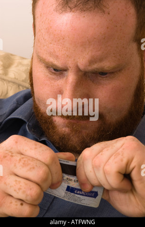 angry young man destroying credit debit bank card to avoid debt and better manage finances Stock Photo