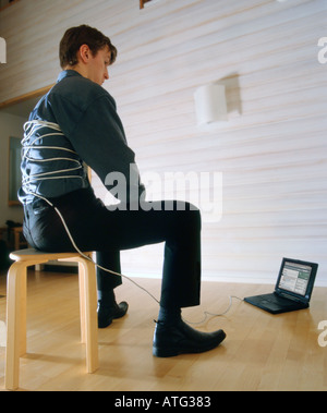 Young man tied to laptop computer with a cable. Concept of internet addiction Stock Photo