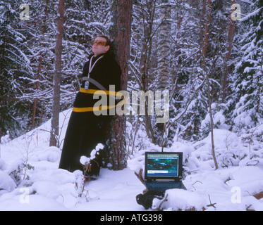 Man in long coat with mobile phone tied to a tree near laptop computer Stock Photo