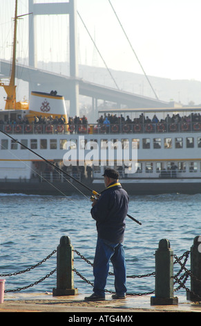 ISTANBUL, TURKEY. Man fishing on the Bosphorus waterfront at Ortakoy, with a ferry and the first Bosphorus bridge behind. 2007. Stock Photo