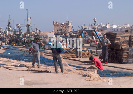 Three men watching others mend fishing nets essaouira port Stock Photo