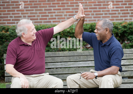 Two businessmen sitting on a bench and giving high five to each other Stock Photo