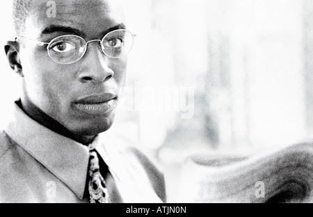 An African American businessman looks up from reading the newspaper Stock Photo