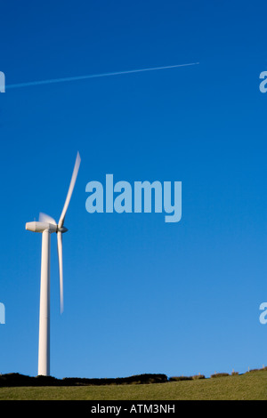 Single wind turbine showing movement against a clear blue sky on a hilltop with a dry stone wall in the foreground Stock Photo